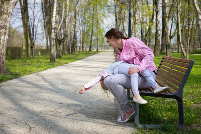 Mother and daughter fooling around while sitting on a bench in a city park.