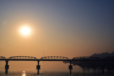 Silhouette bridge over river against sky during sunset