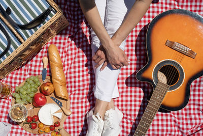Top view of unrecognizable young woman in white pants outside having picnic, eating and playing g