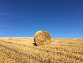 Hay bales on field against clear blue sky