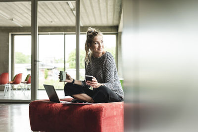 Young businesswoman working in modern office, sitting on stool, using laptop