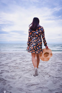 Rear view of woman on beach against sky