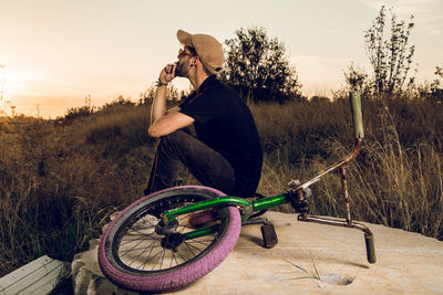 Man holding bicycle by plants against sky during sunset