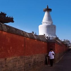 Man walking on street by temple against clear blue sky