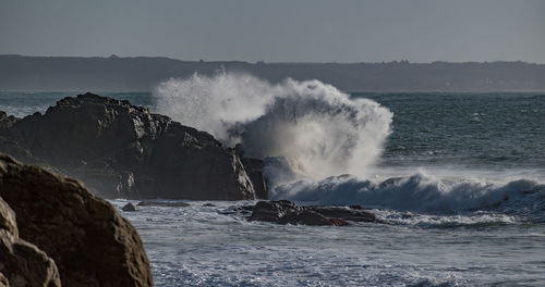 Waves splashing on rocks at shore against clear sky