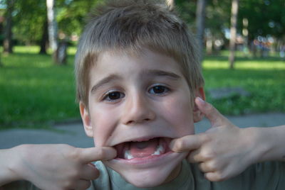 Portrait of cute boy stretching lips in park