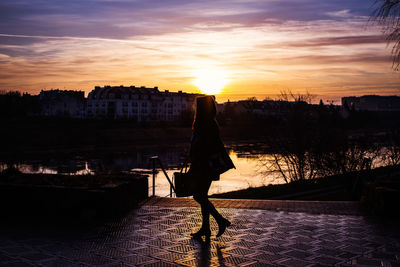 Silhouette woman walking on footpath by lake sky during sunset