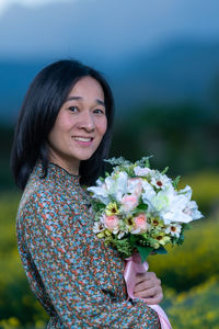 Portrait of smiling woman holding flowering plant