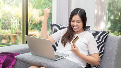 Smiling young woman using mobile phone while sitting at home