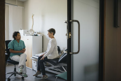 Doctor discussing with female patient seen through doorway in clinic