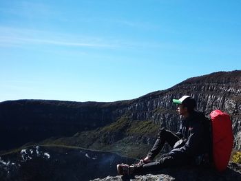 Side view of man sitting on rock against sky