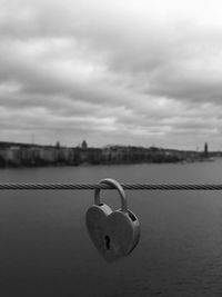 Close-up of padlocks on railing by river against sky