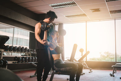 Male fitness instructor instructing woman exercising with dumbbells in gym