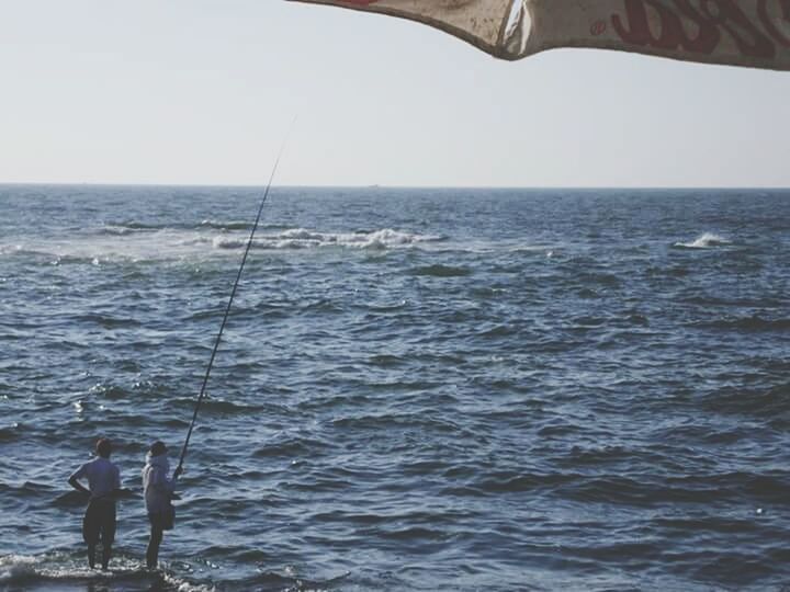 REAR VIEW OF A MAN FISHING IN SEA