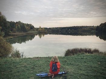 Woman sitting by lake against sky
