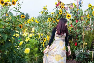 Young woman standing by yellow flowers in field