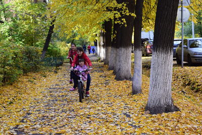 Siblings riding bicycles at park during autumn