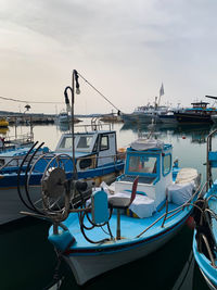 Fishing boats moored at harbor against sky