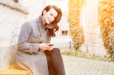 Smiling woman using smart phone while sitting on bench