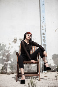 Young woman sitting on chair against weathered wall