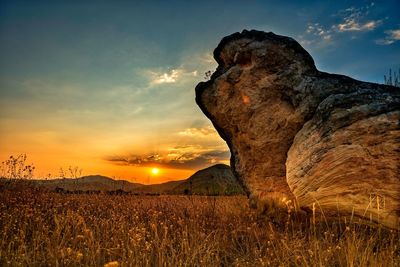 Rock on field against sky during sunset