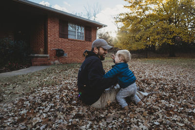 Happy father playing with son while sitting on autumn leaves at yard