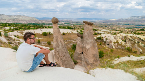 Rear view of woman sitting on rock against sky