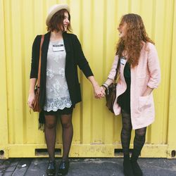 Cheerful friend holding hands while standing against metal wall