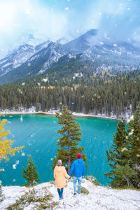 Rear view of woman by lake against mountains during winter