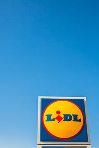 Low angle view of road sign against clear blue sky