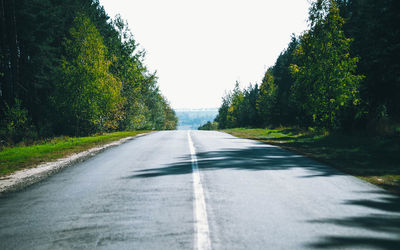 Empty road along trees and against clear sky