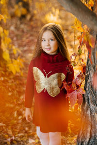 A six-year-old girl in a burgundy knitted tunic walks in autumn in a park with yellow and red leaves