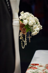 Cropped image of bride holding bouquet and rosary beads during wedding ceremony