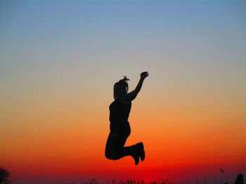 Silhouette man jumping against orange sky