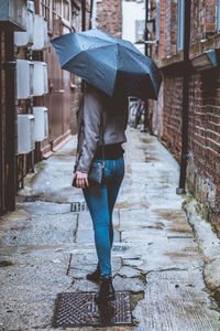 Full length of young woman holding umbrella while standing in alley