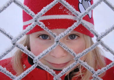 Close-up portrait of teenage girl looking through frozen fence
