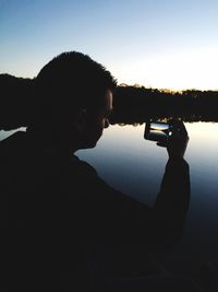 Reflection of man photographing on mobile phone against sky
