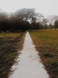 Wet road amidst trees against sky during rainy season