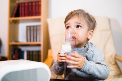 Cute boy inhaling through respiratory machine at home