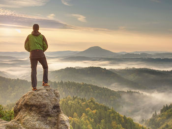 Hiker is standing on sandstone peak in rocky park and watching over misty and foggy morning valley