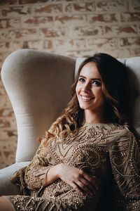 Smiling young woman looking away while sitting on sofa at home