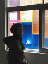 Portrait of young woman standing by window at home