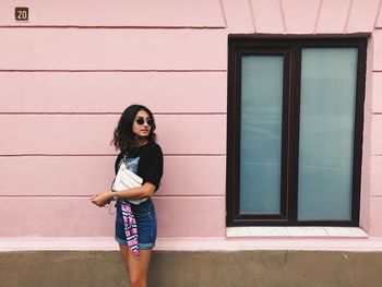 Young woman looking away while standing against wall