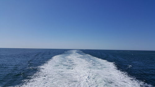 Wake in water against clear blue sky on sunny day