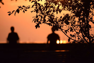Silhouette people standing by tree against orange sky