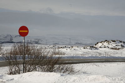 Red sign on snow covered land against sky