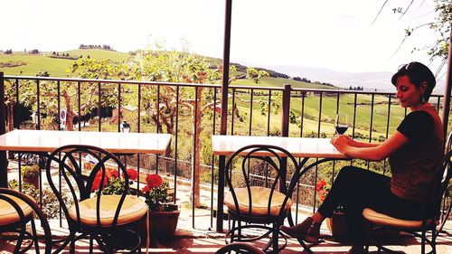 Woman sitting on chair against railing