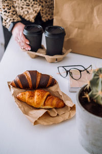 Brown and chocolate croissants and coffee cups, woman having lunch at workplace, food delivery