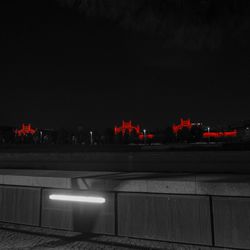 Illuminated road by city against sky at night