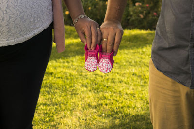 Midsection of pregnant wife with husband holding baby shoes in park
